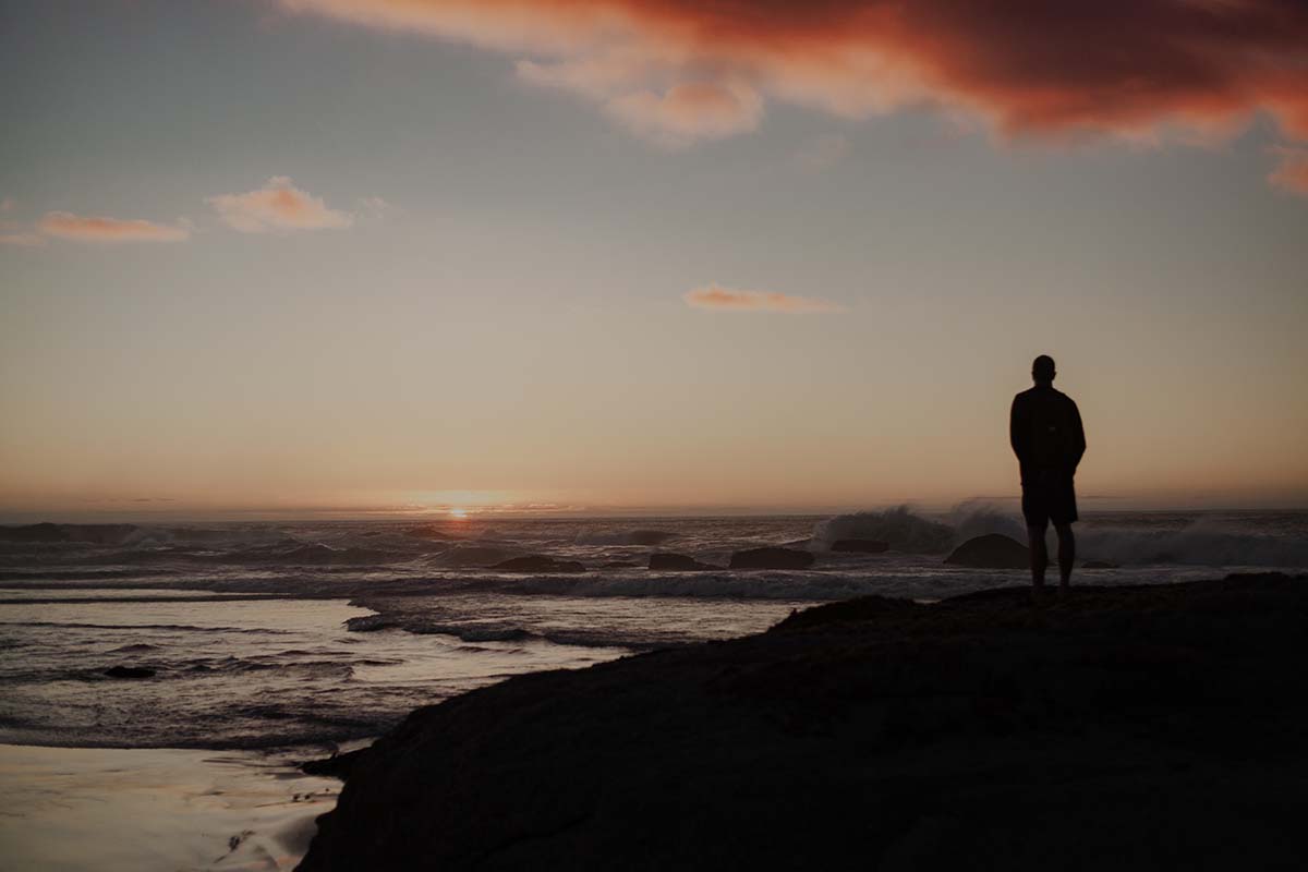 Silhouette of a person standing alone by the ocean at sunset